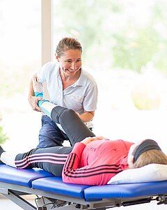 Physiotherapeutin der orthopädischen Reha bei Medical Park hebt das Bein einer Patientin.
