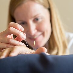 Eine Medical Park Mitarbeiterin führt eine Akupunktur an der Hand eines Patienten durch.