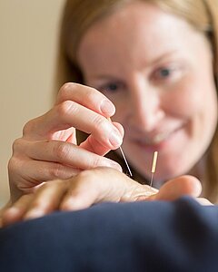 Eine Medical Park Mitarbeiterin führt eine Akupunktur an der Hand eines Patienten durch.