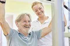 Ein Medical Park Mitarbeiter hilft einem Medical Park Patienten an einem Fitnessgerät.