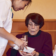 Eine Medical Park Mitarbeiterin verabreicht einer Patientin der orthopädischen Reha Tabletten.